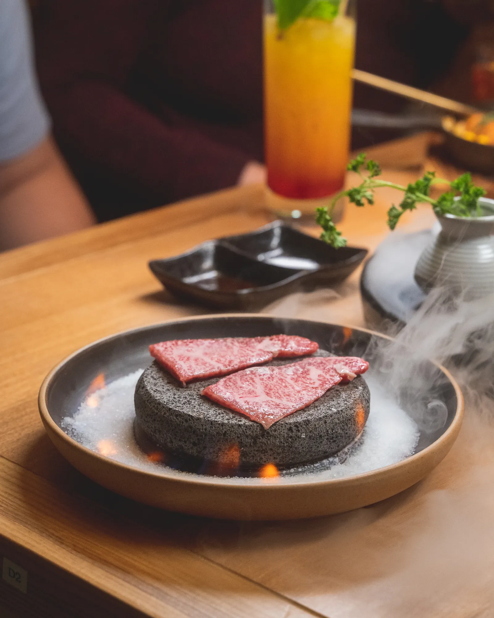 Raw A5 wagyu on a lava hot stone over salt, glowing embers and drifting smoke