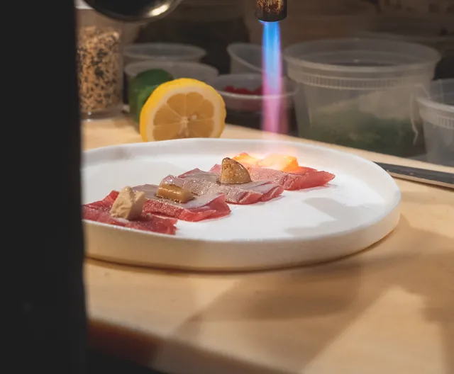 A chef’s torch searing tuna at Genki