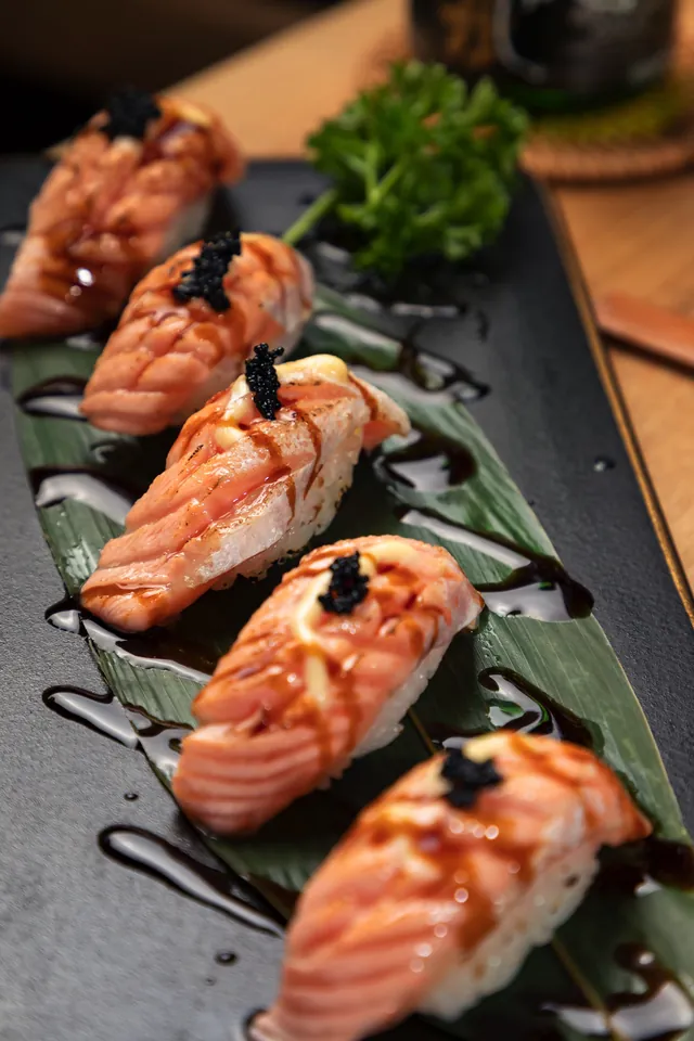 Torched salmon nigiri arranged on a dark serving plate